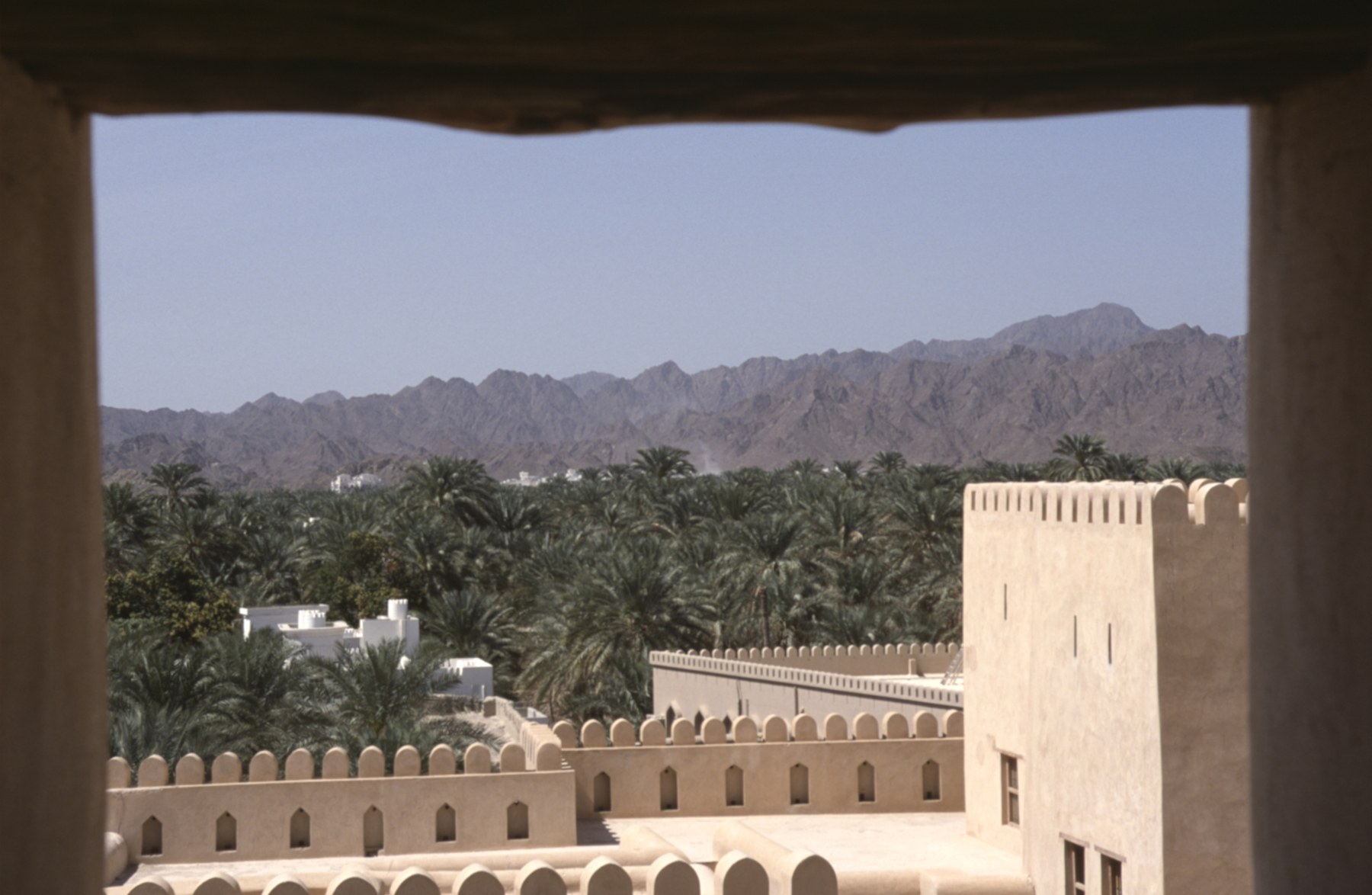 Blick aus der Festung von Nizwa auf Wehrmauern, Palmen und Berge